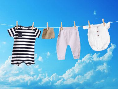 Mavi gökyüzüne karşı çamaşır ipinde kurumuş farklı bebek kıyafetleri.
