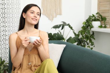 Uyum. Bir fincan sıcak içecekle gülümseyen kadın evdeki kanepede dinleniyor.