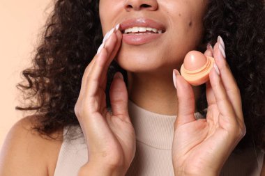 Bej arka planda dudak kremi olan gülümseyen kadın, yakın plan.