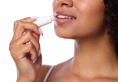 Gülümseyen kadın dudaklarına merhem sürüyor. Beyaz arka planda, yakın plan.