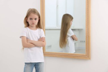 Evdeki aynanın yanındaki üzgün küçük kız.