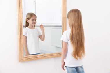 Güzel küçük kız aynada kendine bakıyor.