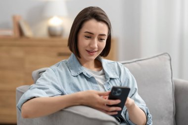 Evdeki koltukta modern akıllı telefon kullanan bir kadın.