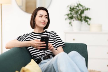 Evdeki koltukta modern akıllı telefon kullanan bir kadın. Metin için boşluk