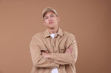 Açık kahverengi arka planda bej renkli beysbol şapkası giyen genç bir adam.