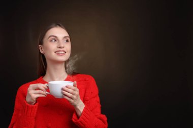 Kahverengi arka planda bir fincan kahveyle gülümseyen kadın. Metin için boşluk