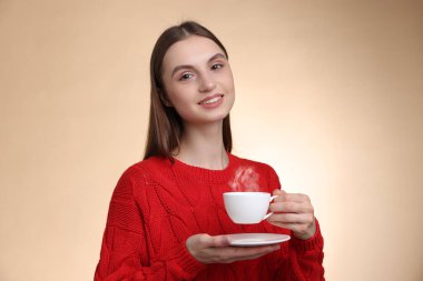 Bej renkli arka planda bir fincan kahveyle gülümseyen kadın