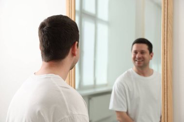 Yakışıklı adam aynada kendine bakıyor.