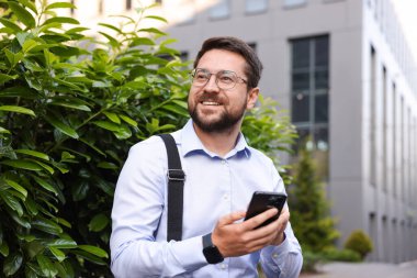 Ofis binası yakınında akıllı telefonu olan başarılı bir iş adamı.