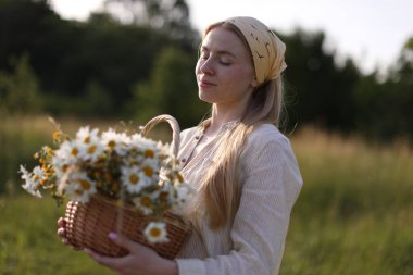 Açık havada sepet dolusu kır çiçeğiyle mutlu bir kadın.