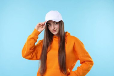 Açık mavi arka planda şık bir beyzbol şapkası takmış güzel bir kadının portresi.