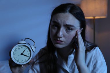 Evde uykusuzluk çeken, çalar saati olan, hayal kırıklığına uğramış bir kadın.