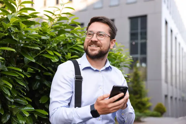 Ofis binası yakınında akıllı telefonu olan başarılı bir iş adamı.