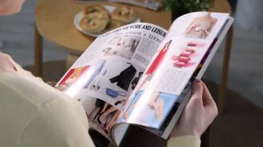 Kadın evde yaşam tarzı dergisi okuyor, yakın çekim manzarası var.