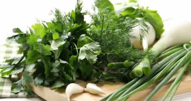 Farklı taze otlar, yeşil soğanlar ve beyaz ahşap masada sarımsak, yakın plan.