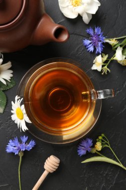 Cam bardakta Aromatik bitki çayı, farklı çiçekler ve siyah masada çaydanlık, düz uzanmış