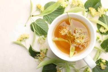 Taze ıhlamur çayı fincanda ve çiçekler beyaz masada, düz yerde.