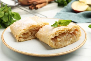 Lezzetli elmalı turta parçaları pudra şekeri, nane, meyve ve tarçın beyaz mermer masada, yakın plan.