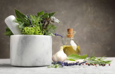 Topuzlu havan, farklı aromatik otlar ve baharatlar gri masada, yakın plan. Metin için boşluk