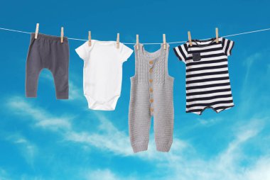 Mavi gökyüzüne karşı çamaşır ipinde kurumuş farklı bebek kıyafetleri.
