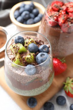 Gri masadaki bardaklarda Chia tohumu ve böğürtlen bulunan lezzetli çikolatalı pudingler.