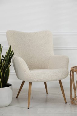 Rahat koltuk, yan masa ve beyaz duvarın yanındaki bitki örtüsü.