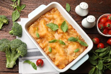 Pişirme kabında leziz vejetaryen lazanya ve ahşap masada malzemeler.