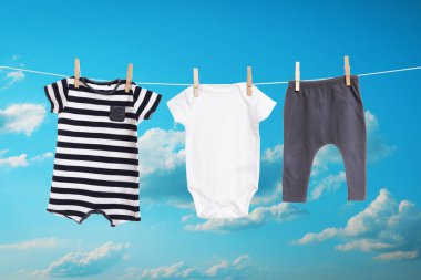 Mavi gökyüzüne karşı çamaşır ipinde kurumuş farklı bebek kıyafetleri.