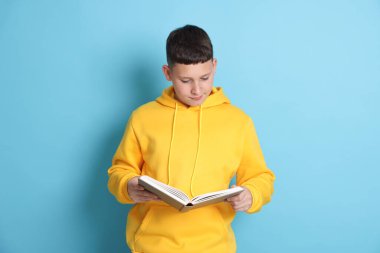 Genç çocuk açık mavi arkaplan üzerine kitap okuyor.