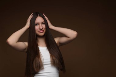 Kahverengi arka planda sağlıklı uzun saçlı güzel bir genç kızın portresi. Metin için boşluk