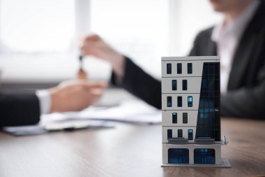 Emlakçı ofisteki müşteriye anahtarı veriyor, ev modeline odaklanıyor.