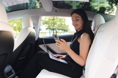 Modern arabada akıllı telefonu ve bilgisayarı olan bir kadın.