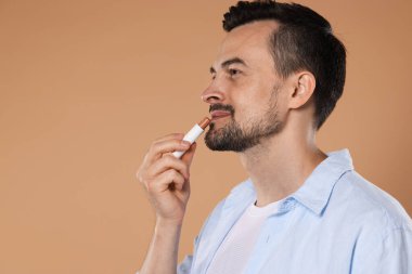 Açık kahverengi arka planda dudaklarına dudak kremi süren yakışıklı bir adam. Metin için boşluk