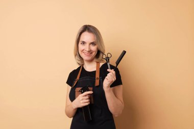 Bej arka planda tarak, makas ve sprey şişesiyle gülümseyen kuaför.