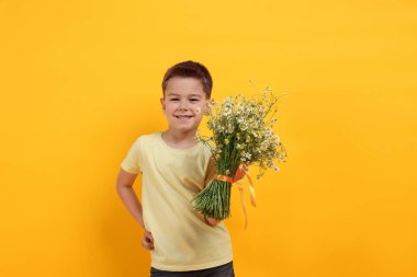 Sarı arka planda bir buket güzel papatya çiçeğiyle gülümseyen küçük çocuk