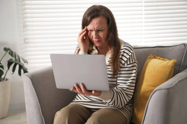 Evdeki koltukta dizüstü bilgisayar kullanan görme sorunu olan bir kadın.