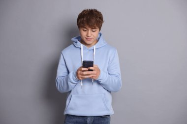 Genç çocuk gri arka planda akıllı telefon kullanıyor.