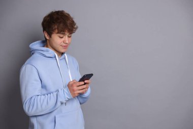 Genç çocuk gri arka planda akıllı telefon kullanıyor. Metin için boşluk