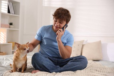 Gülümseyen genç çocuk evde akıllı telefon ve köpekle konuşuyor.