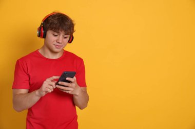 Kulaklıklı genç çocuk sarı arka planda akıllı telefon kullanıyor. Metin için boşluk