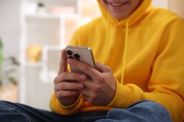 Gülümseyen genç çocuk evde akıllı telefon kullanıyor, yakın plan.