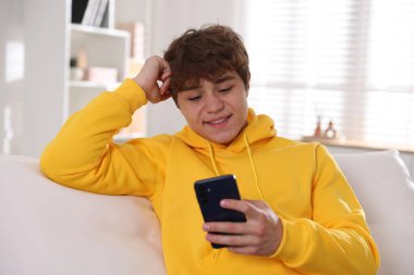 Evdeki kanepede akıllı telefon kullanan gülümseyen genç çocuk.