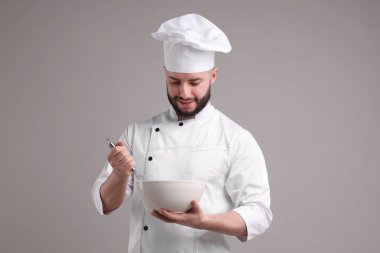 Üniformalı mutlu pastacı açık gri arka planda çırpı ve kase tutuyor.