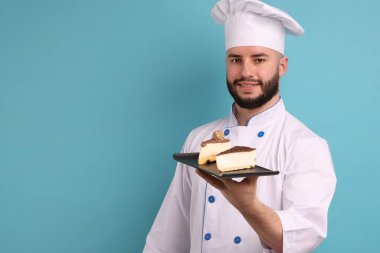 Üniformalı mutlu pastacı elinde açık mavi arka planda lezzetli peynirli kek parçaları tutuyor.