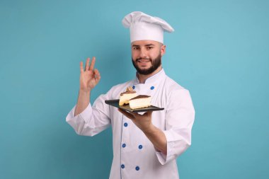 Üniformalı mutlu pastacı elinde lezzetli cheesecake parçaları tutuyor ve açık mavi arka planda güzel bir jest yapıyor.