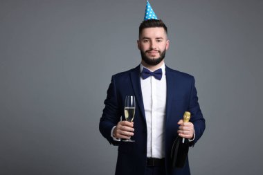 Doğum günün kutlu olsun. Gri arka planda parti şapkası ve şampanyası olan yakışıklı bir adam.