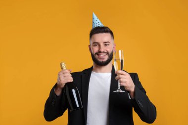 Doğum günün kutlu olsun. Turuncu arka planda parti şapkası ve şampanyası olan yakışıklı adam.