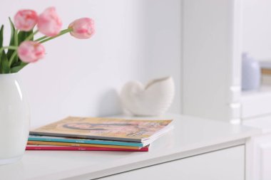 Beyaz dolaptaki birçok modaya uygun dergi ve lale çiçekleri, yakın plan.