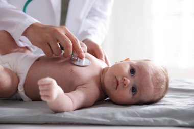 Klinikteki masada steteskopla bebeği muayene eden çocuk doktoru.