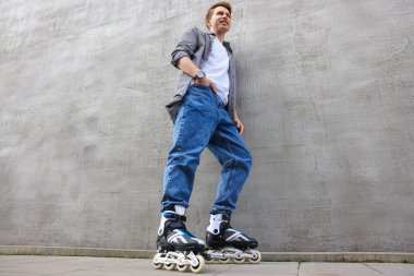 Gri duvarın yanında patenli mutlu genç adam, alçak açılı manzara.